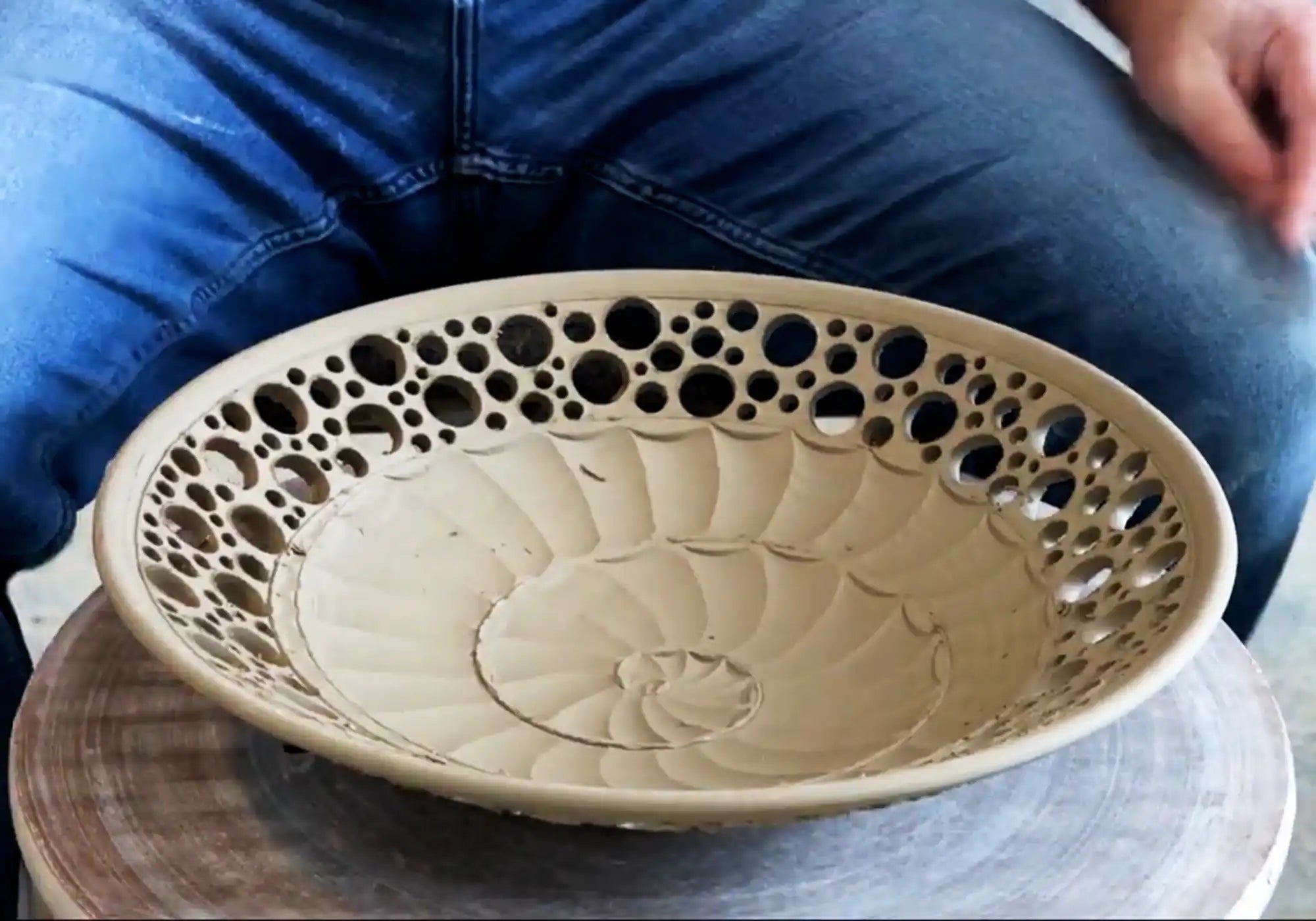 A handmade bowl, still somewhat soft clay, sitting on a potter's wheel after being carved by the potter who made it.