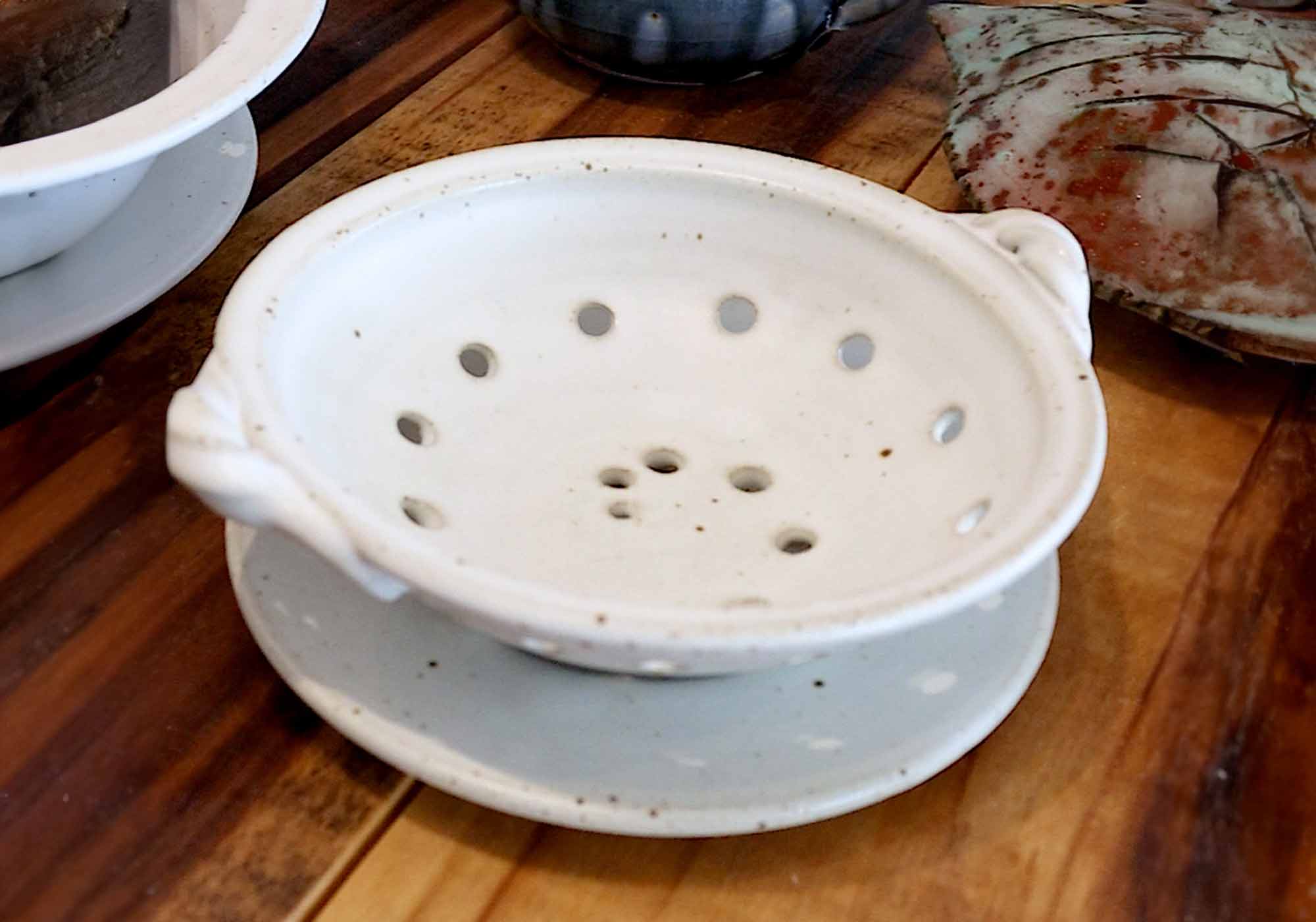 A small handmade ceramic berry bowl with a satin white glaze, sitting on a wooden table.