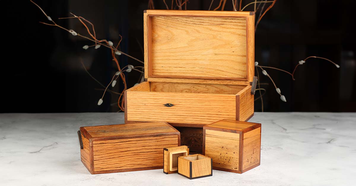 A small vignette of handmade wooden boxes by Alan Darveaux, sitting on a light-colored surface with a background fading into darkness.