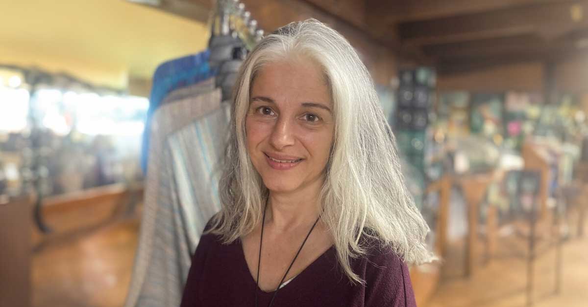 A smiling, white-haired older woman standing in a retail space at Crossnore Weavers