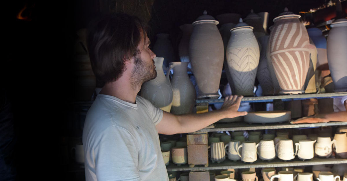 A young man, Curry Wilkinson, looking at a collection of pots that are setting in a large wood kiln waiting to be fired.