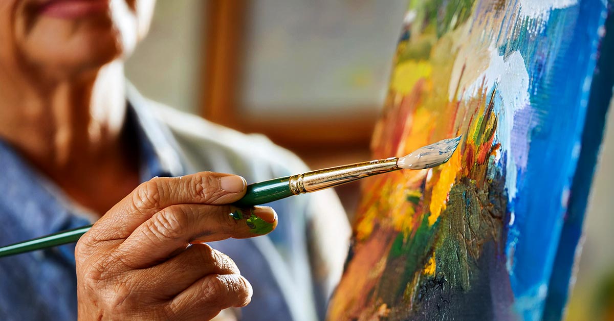 A painter's hand holds a brush against a canvas full of color.